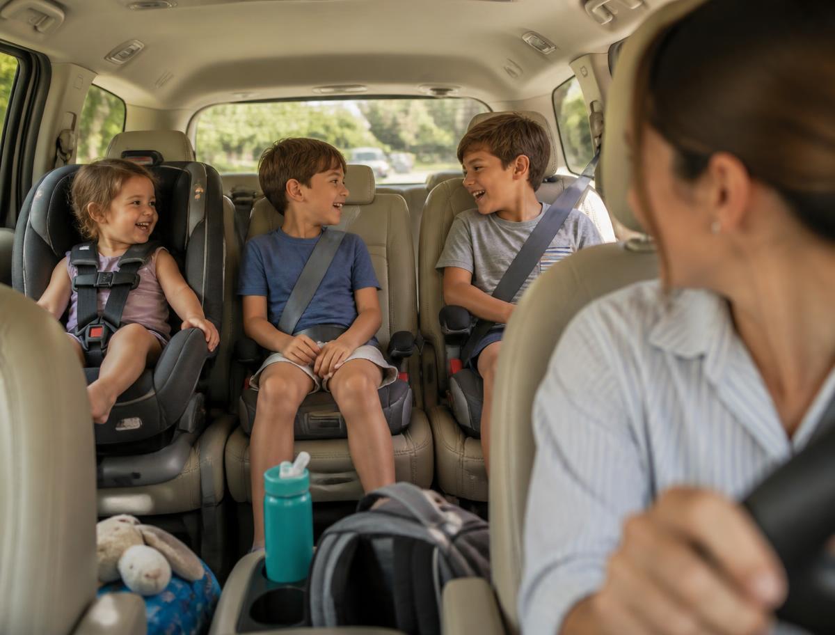 Mom driving a minivan with three children buckled in the back seats listening together